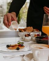 a person pouring syrup onto a plate of food at Hotel Vier Jahreszeiten Starnberg in Starnberg