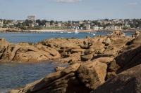 a group of rocks on the water with a city at La plage in Trébeurden