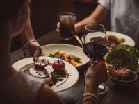 Personas sentadas en una mesa con platos de comida y una copa de vino. en Horizon by SkyCity, en Auckland