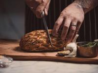 una persona cortando un pan con un cuchillo en una tabla de cortar en Horizon by SkyCity, en Auckland