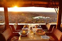 uma mesa com dois pratos de comida e taças de vinho em Victoria Falls Safari Suites em Victoria Falls