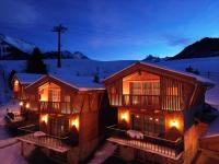 two log homes with lights on them in the snow at Bergdorf Hotel Zaglgut in Kaprun
