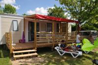a tiny house with a red roof and two people sitting in a chair at Camping La Mignardière in Ballan-Miré