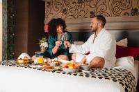 a man and woman sitting on a bed with a tray of food at Van Der Valk Sélys Liège Hotel &amp; Spa in Liège