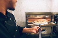 a man is putting a pizza in an oven at Gspot Hostels & Love Triangles Pizzeria in Lisbon
