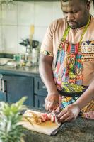 KinigiKinigi Cottage的坐在厨房里的人在切板上准备食物