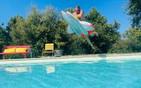 a man is jumping into a swimming pool with a inflatable shark at Le Planzollais in Planzolles