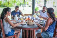 Un grupo de personas sentadas alrededor de una mesa comiendo comida en Pousada Sargi&mar, en Uruçuca