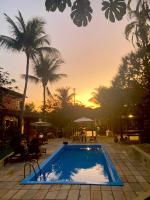a pool with palm trees and a sunset in the background at Hotel Pousada Marambaia in Arraial d'Ajuda