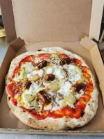 eine Pizza, die in einer Kiste auf einem Tisch sitzt in der Unterkunft Aux Chambres du Mont in Huisnes-sur-Mer