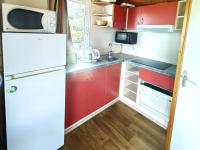 a small kitchen with red cabinets and a white refrigerator at Chalet Agde, 3 pièces, 6 personnes - FR-1-607-59 in Agde