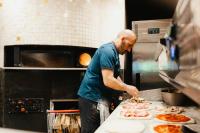 a man making pizzas in a kitchen at Camping Fuussekaul in Heiderscheid