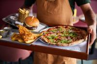 un uomo che tiene in mano un vassoio con una pizza, un hamburger e delle patatine fritte di Thistle London Heathrow Terminal 5 a Hillingdon
