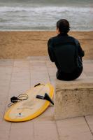 a man sitting on a ledge next to a surfboard at ALFRED HOTELS Les Halles - Ex Hotel Anjou in Biarritz