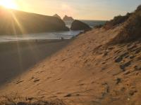 a sandy beach with the sun rising over the ocean at Relax in style at my stunning Holywell Beach home in Holywell Bay