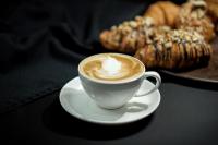 a cup of coffee on a white plate with a pastry at The Alcor Hotel in Jamshedpur