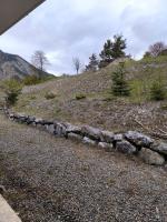 a stone retaining wall on a hill with trees at studio tout équipé in Jausiers