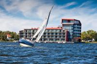 a sail boat in the water in front of a building at Hotel Mikołajki Leisure &amp; SPA - Destigo Hotels in Mikołajki