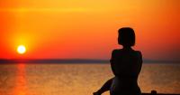 una mujer sentada en la playa mirando la puesta de sol en Hilltop Serenity Villa, en Imerovigli