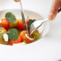 una persona que sostiene un tenedor y un cuchillo sobre un tazón de fruta en Logement The Black Tie, en Assen