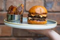 una persona sosteniendo un plato con una hamburguesa y papas fritas en The Haughmond, en Shrewsbury