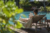 a woman sitting in a chair reading a book by a pool at Stay Wellbeing & Lifestyle Resort in Rawai Beach