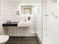 a white tiled bathroom with a sink and a toilet at Mercure Cardiff North Hotel in Cardiff