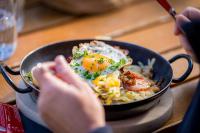 Una persona que sostiene una sartén con comida y huevos encima. en Hotel Restaurant Berghaus Malbun Buchserberg, en Buchs