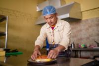 a man in a kitchen preparing a pizza on a plate at Nepali Heritage Hotel in Kathmandu