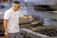 a man in a kitchen preparing food on a grill at JetPark Auckland Airport Hotel in Auckland