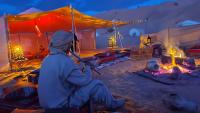 a person sitting in front of a tent with a fire at CAMP ABDELMOULA in Douz