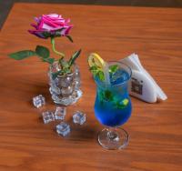 Un jarrón con una rosa y una bebida azul sobre una mesa. en فندق المدى العربية الفندقية, en Jazan