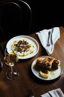 パースにあるパーメリア ヒルトン パースの2枚の皿に盛られた料理とグラス一杯のワインが置かれたテーブル