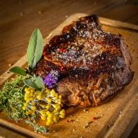 a piece of steak on a cutting board with flowers at Hôtel SPA du Lac de Madine - Maison DRAPIER in Heudicourt-sous-les-Côtes