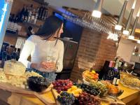 Una mujer sosteniendo una copa de vino detrás de una mesa de frutas. en Pensiunea Senin, en Sovata