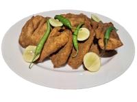 Un plato de pollo frito con pimientos verdes y rodajas de limón. en Ceylon Kingsmen Garden - Katunayake Airport Transit Hotels, en Negombo