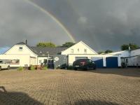 Un arcoíris sobre una casa con un coche aparcado en la entrada. en tauwerk Hotel, en Wilhelmshaven