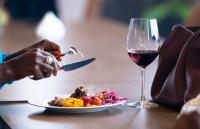 una persona cortando un plato de comida con una copa de vino en Trademark Suites at Enaki Town, en Nairobi