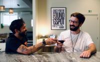 two men sitting at a table with a glass of wine at Gspot Hostels & Love Triangles Pizzeria in Lisbon