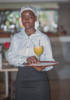 a woman holding a tray with a drink on it at Hôtel La Rose Blanche Abidjan in Abidjan