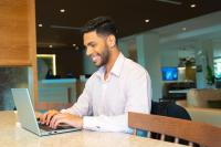 un hombre sentado en una mesa usando un ordenador portátil en Fairfield by Marriott Luquillo Beach, en Luquillo