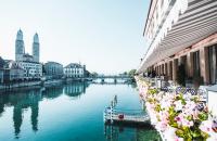 a view of a river with buildings and flowers at Storchen Zürich - Lifestyle Boutique Hotel in Zürich