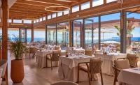 Un restaurante con mesas y sillas blancas y grandes ventanales. en Universal Grand León & Spa, en Colonia de Sant Jordi