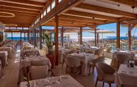 Un restaurante con mesas y sillas blancas y ventanas. en Universal Grand León & Spa, en Colonia de Sant Jordi