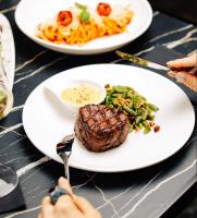 Una mesa cubierta con platos de comida con bistec y verduras. en Luxor Hotel & Casino, en Skopje