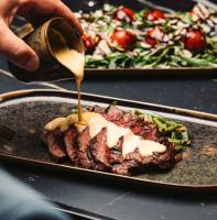 una persona rociando salsa sobre un filete en un plato en Luxor Hotel & Casino, en Skopje