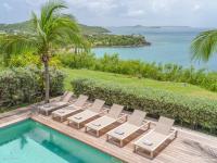 a pool with lounge chairs and the ocean at Be Happy à pied de Friar's Bay face au coucher de soleil in Friar's Bay
