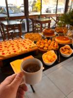 マカコスにあるPousada Vilarejoの食べ物のテーブルの前でコーヒーカップを持っている人