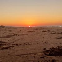 a sunset on a beach with the sun setting in the distance at Camping rock in Itanhaém
