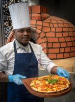 a man holding a pizza on a wooden board at Okash City Boutique Hotel in Nairobi